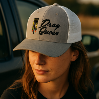 Woman wearing a heather grey and white embroidered trucker cap featuring a drag-racing light tree and “Drag Queen” text — Geaux Big motorsport lifestyle photo.