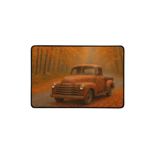 Small 12×18 inch desk mat featuring a vintage pickup truck on an autumn forest road with black hemmed edges.