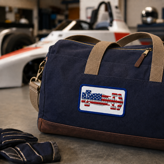 USA flag formula racing car embroidered patch displayed on a navy duffel bag in a motorsport-inspired garage setting.